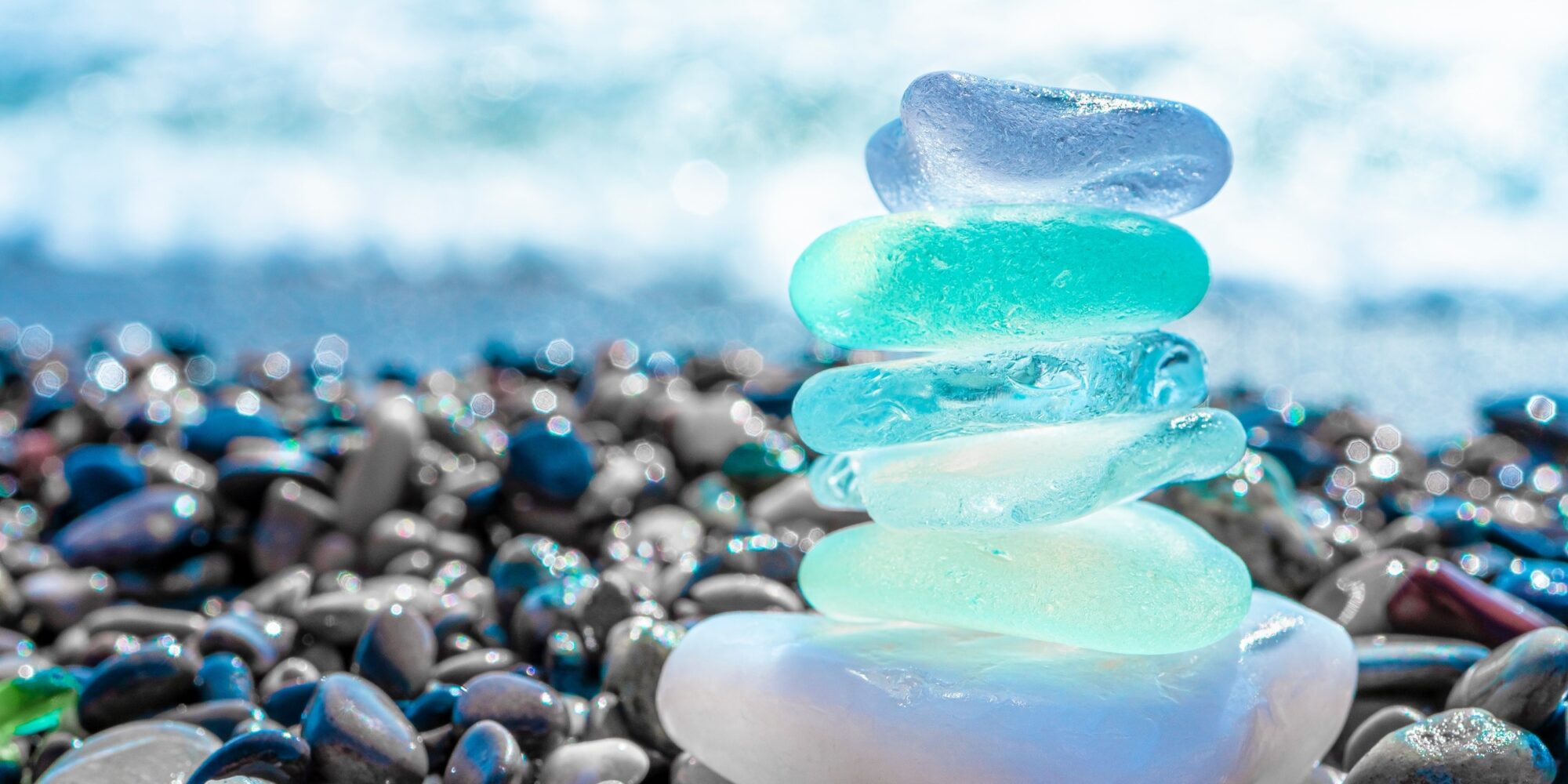 Sea glass stones arranged in a balance pyramid on the beach. Beautiful azure color sea with blurred seascape background. Meditation and Harmony concept